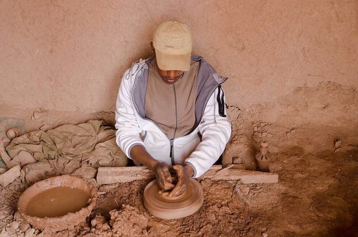 A person working on a pottery wheel in a rustic setting.