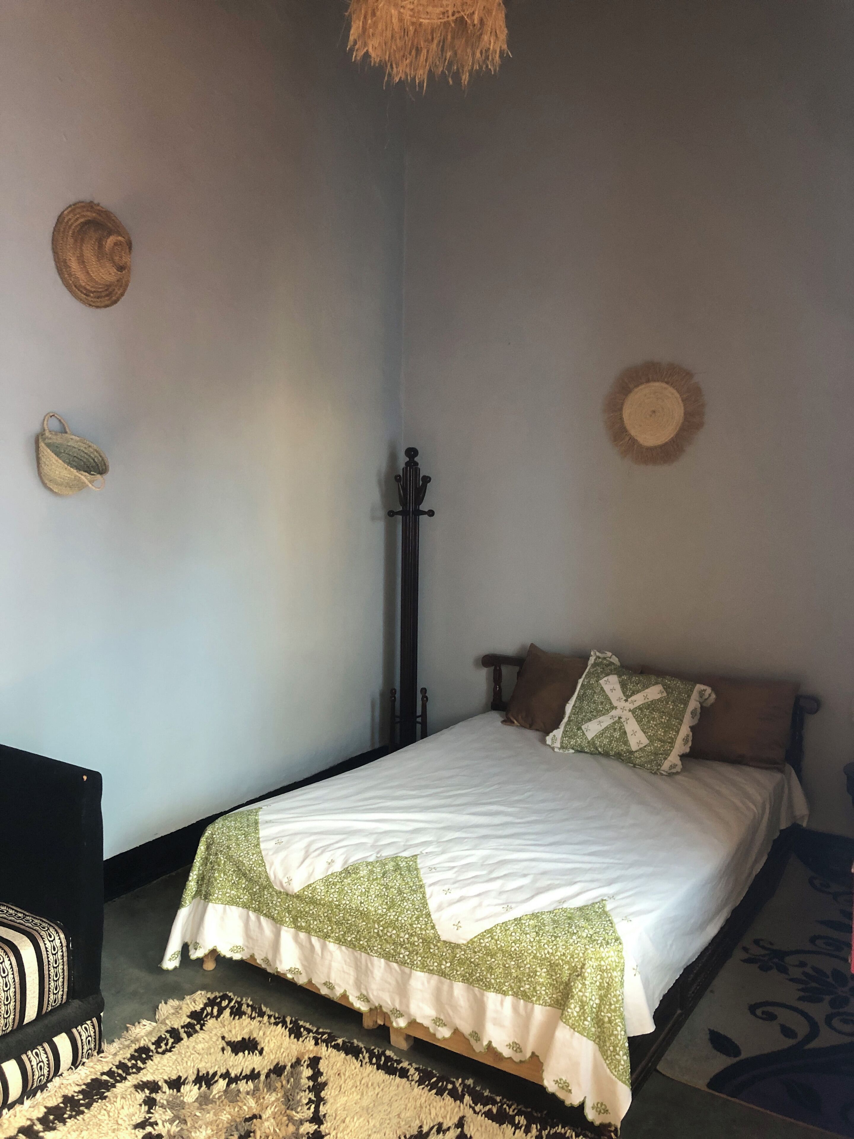 Un dormitorio con cama, una mesita de noche de madera, una cesta tejida y un adorno en la pared.