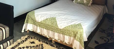Un dormitorio con cama, una mesita de noche de madera, una cesta tejida y un adorno en la pared.