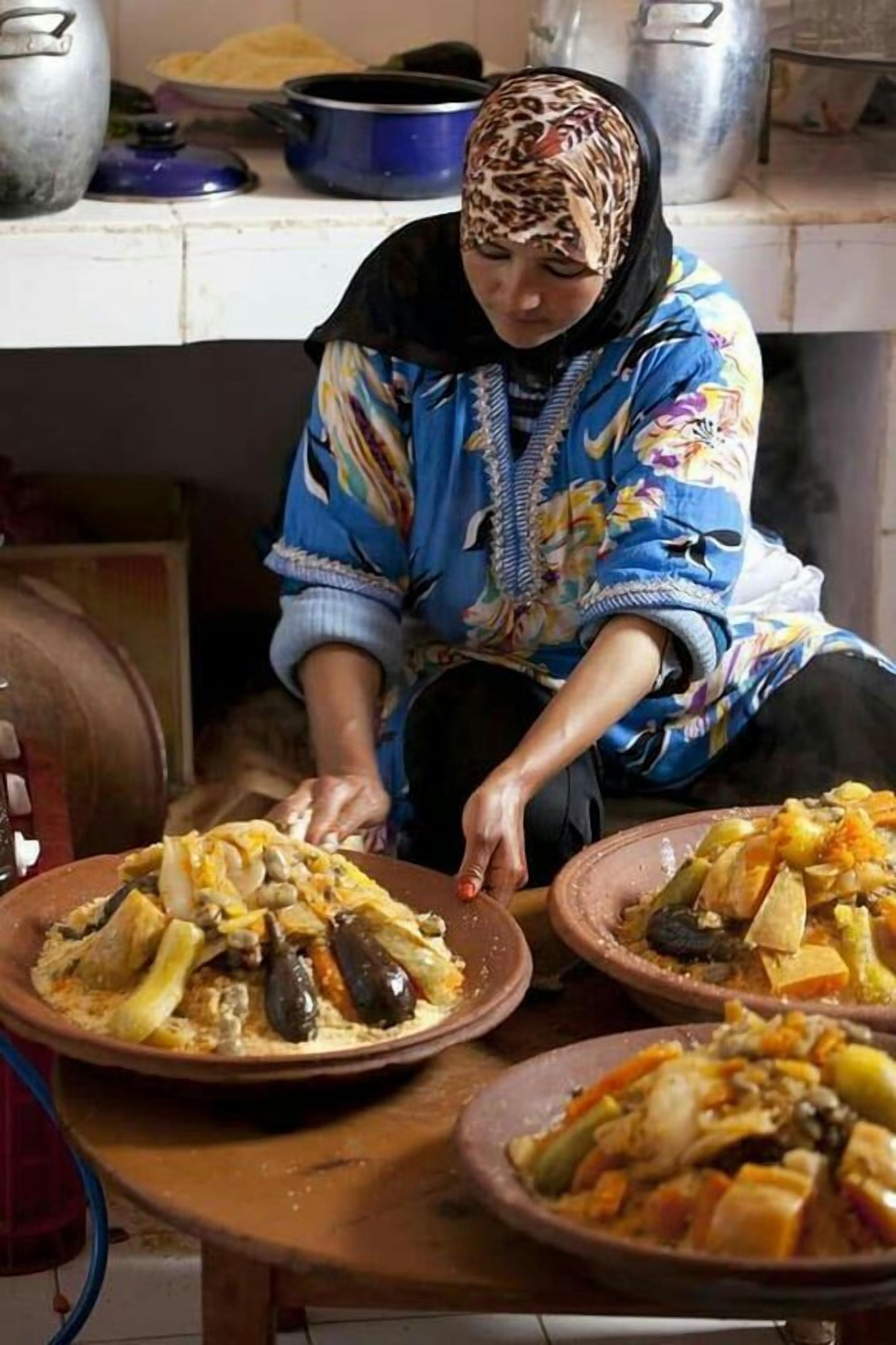 A person preparing food in a kitchen with large pots and a variety of dishes on the table.