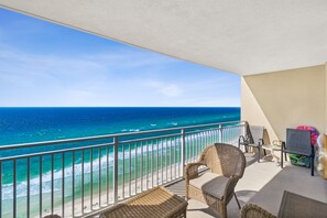 Een balkon met rieten meubilair, uitzicht op de oceaan en een strand op de achtergrond.