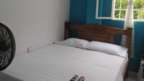 A small, single-bed room with a wooden headboard, a white bedspread, and a fan on the left. - 7 min. from the most beautiful beach in Colombia, El Rodadero, Santa Marta, Colombia. (SANTA MARTA)