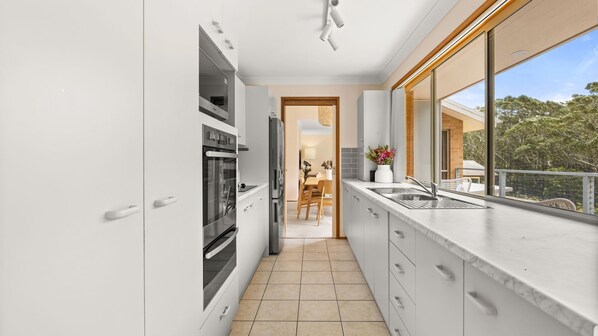 A modern kitchen with white cabinets, stainless steel appliances, and a large window overlooking a balcony.