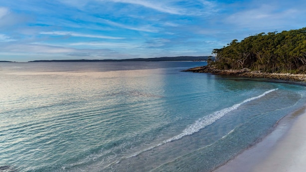 A beach with clear turquoise water, a sandy shore, and a forested area in the background. - White Sands House by Experience Jervis Bay (Vincentia)