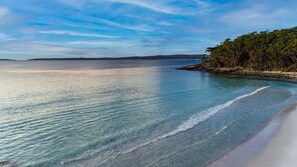 A beach with clear turquoise water, a sandy shore, and a forested area in the background.