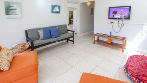 Ein Wohnzimmer mit grauem Sofa, orangefarbenem Sofa, Wand-Fernseher und kleinem Holztisch mit einer Zeitschrift.