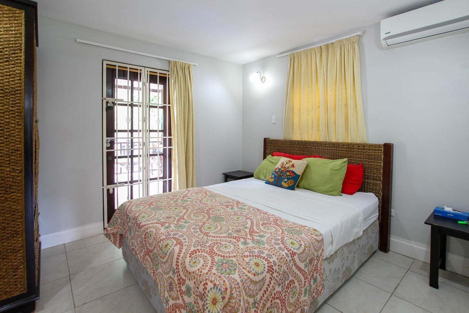 Une chambre à coucher comprenant un lit, une table de chevet, une fenêtre avec des rideaux et un appareil de climatisation.