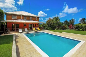 A pool with a wooden deck, a red building with a metal roof, and a clear blue sky.