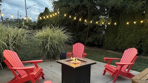 Een terras met een vuurkuil, rode Adirondack-stoelen en lichtjes.