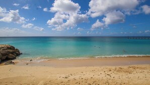Een strand met helder turquoise water, een zandstrand en een rotsachtige landtong.