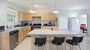 Een moderne keuken met granieten aanrechtbladen, houten kastjes en roestvrijstalen apparatuur, plus barkrukken.