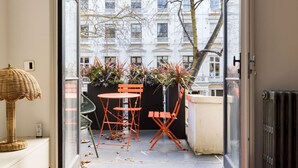 A balcony with a table and chairs, potted plants, and a wicker lamp.