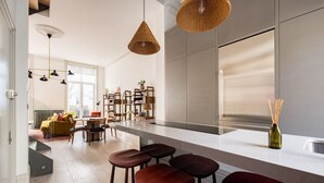 A modern kitchen with a large island, bar stools, and a dining area with a yellow sofa.