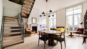 A modern living room with a wooden staircase, a dining area, and large windows.