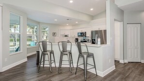 A modern kitchen with white cabinetry, stainless steel appliances, and a bar area with metal stools. - Enjoy this lovely updated 4-bedroom, 2.5-bath waterfront home 2.5 miles from Tigertail Beach (Marco Island)