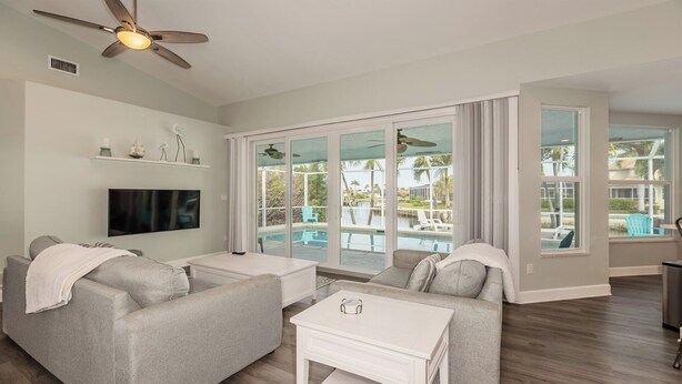 A spacious living room with a flat-screen TV, two grey sofas, a coffee table, and a ceiling fan. - Enjoy this lovely updated 4-bedroom, 2.5-bath waterfront home 2.5 miles from Tigertail Beach (Marco Island)