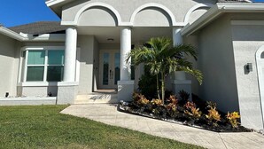 A modern two-story house with a front porch, a covered entryway, and a landscaped garden with palm trees and shrubs. - Enjoy this lovely updated 4-bedroom, 2.5-bath waterfront home 2.5 miles from Tigertail Beach (Marco Island)