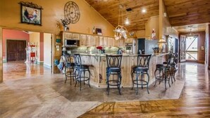A spacious kitchen with a central island, bar stools, wooden ceiling, and a large clock on the wall. - Luxurious farm house! 5-bed, 4 bath, with pool. (Bonham)