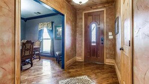 A hallway with wooden walls and a wooden door. There is a rug on the floor and a chair in the background. - Luxurious farm house! 5-bed, 4 bath, with pool. (Bonham)