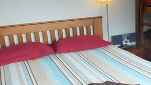 Una cama con una colcha a rayas, dos almohadas rojas y una toalla oscura.