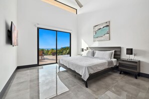 A modern bedroom with a large bed, a nightstand, a TV, and a painting. - Luxury 6 Bedroom Villa w/full gym. Ocean View- Luxury Finishes -Gated Community (Tamarindo)