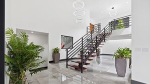 Un interior moderno con una escalera, plantas en macetas y un suelo pulido.