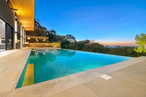 A modern pool with a clear blue water surface, surrounded by a paved deck and a wooden pergola. - Luxury 6 Bedroom Villa w/full gym. Ocean View- Luxury Finishes -Gated Community (Tamarindo)