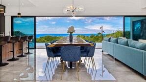 Un comedor moderno con una mesa grande, sillas azules y vista al océano.