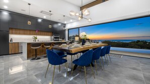 Una cocina moderna con una isla grande, armarios oscuros y vistas del atardecer a través de un ventanal amplio.