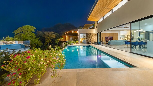 Una casa moderna con piscina, mobiliario exterior y un amplio ventanal de vidrio.