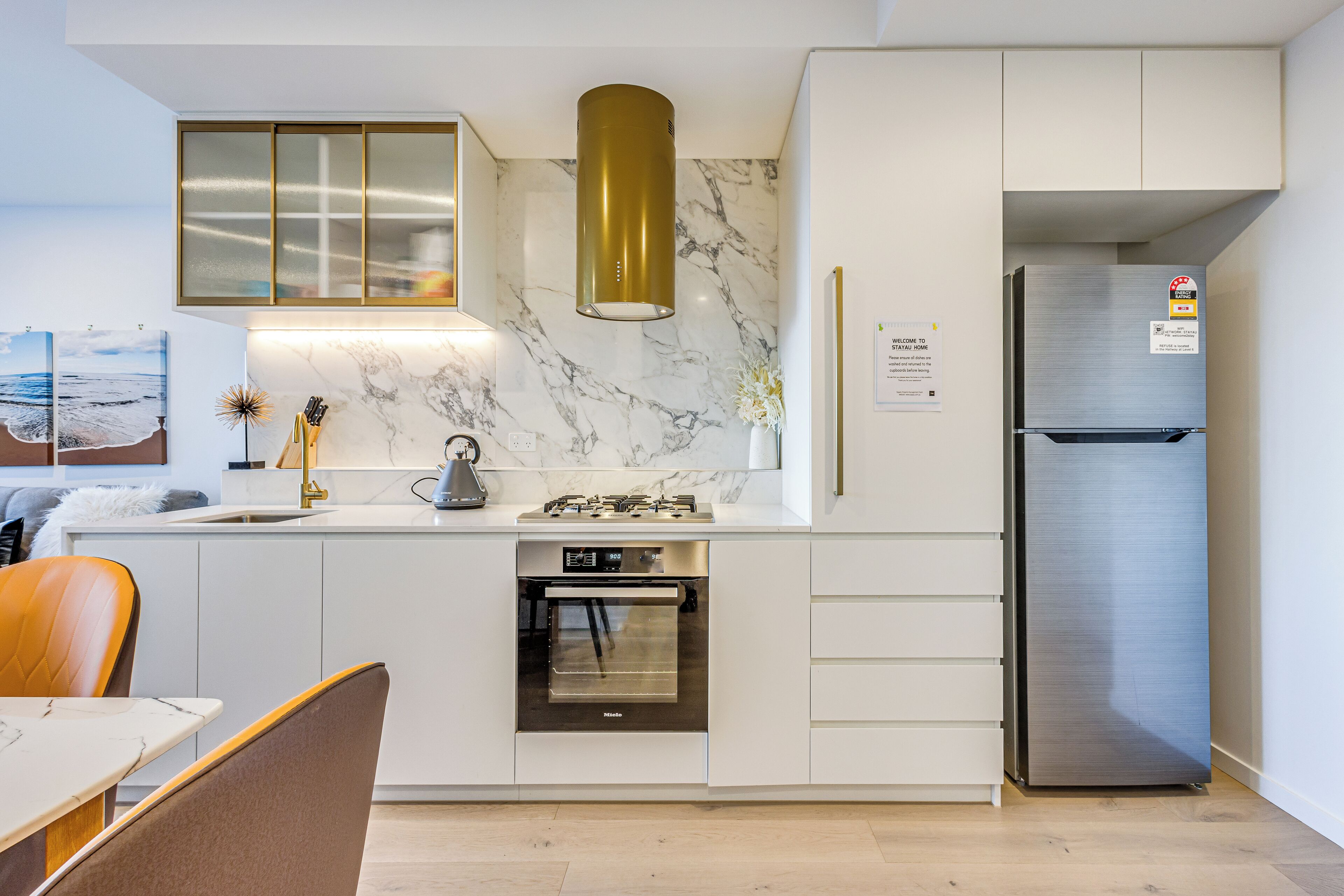 Eine moderne Küche mit weißen Schränken, einem Edelstahlkühlschrank, einem Einbauofen und einer Marmor-Spritzschutzwand.