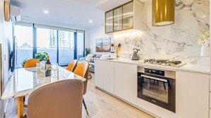 Una cocina moderna con horno integrado, una zona de comedor con mesa y sillas, y un ventanal con vistas a la ciudad.