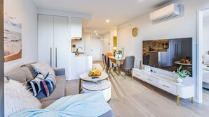Una sala de estar moderna con un sofá, una mesa redonda de centro y un televisor. Hay una zona de cocina con una mesa de comedor y sillas.