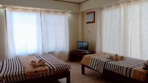 Habitación de hotel con dos camas, un televisor sobre una mesita y una ventana con cortinas.