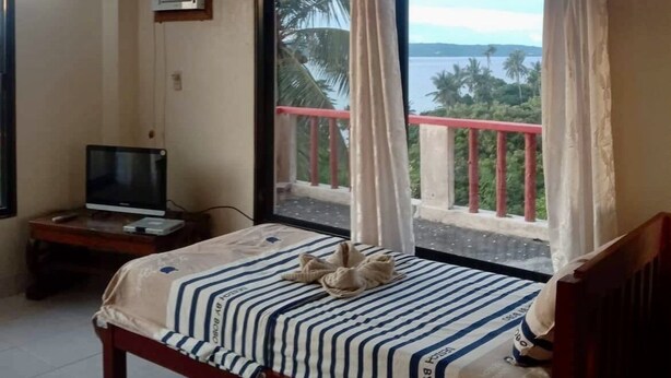 Habitación de hotel con cama, televisor sobre un mueble bajo y balcón con vista al mar.