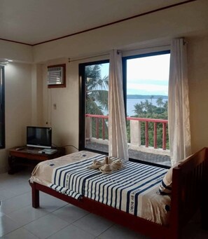 Habitación de hotel con cama, televisor sobre un mueble bajo y balcón con vista al mar.