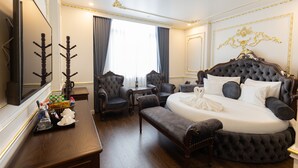 Une chambre à coucher luxueuse avec un grand lit, un coin salon avec des fauteuils, une petite table et un miroir.