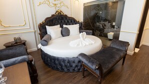 Une chambre à coucher luxueuse avec un grand lit rond, une coiffeuse avec un miroir et un coin salon comprenant deux fauteuils.