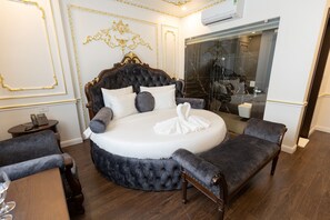 Relax in this serene bedroom with a large round bed, tufted headboard, and dark blue bench.