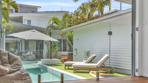Un área exterior moderna con piscina, sillas de descanso y un espacio cubierto con vidrio.