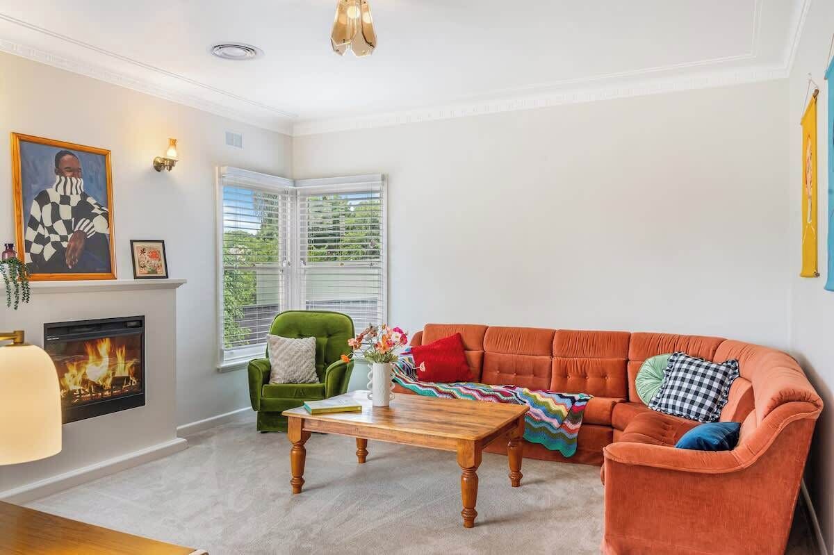 A living room with a fireplace, a green armchair, an orange sofa, and a wooden coffee table.