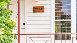 Una porta blanca amb un senyal de fusta que diu “TARA” a dalt, una reixa de metall vermella i una finestra amb un dibuix de rejilla.