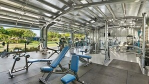 Ein überdachter Fitnessraum mit verschiedenen Trainingsgeräten, darunter Bänke und Kraftmaschinen.
