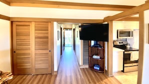 Ein Flur, der zu einer Küche mit Fernseher, Holzboden und einer Schiebetür führt.