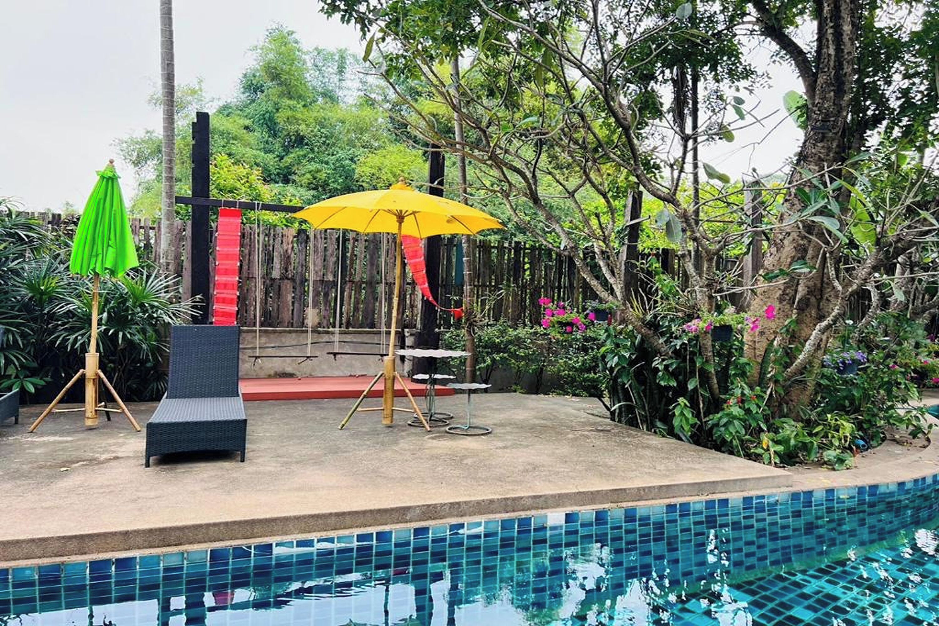 A poolside area with a wooden fence, a yellow umbrella, and a black lounge chair.