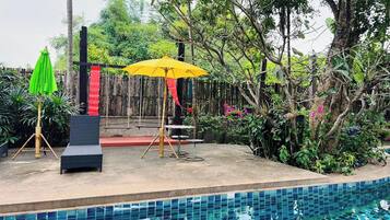 A poolside area with a wooden fence, a yellow umbrella, and a black lounge chair.