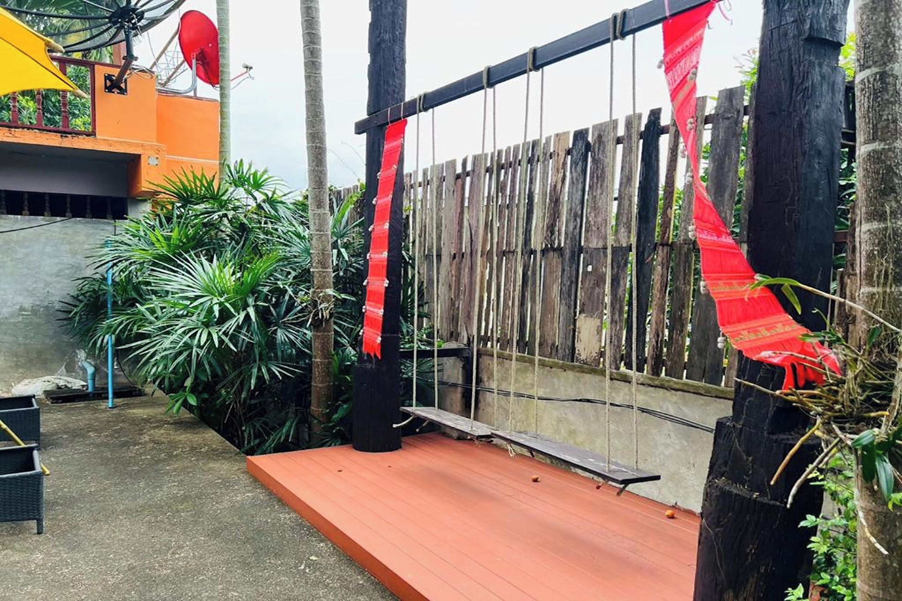 A wooden fence with red fabric decorations, a concrete floor, and green plants.