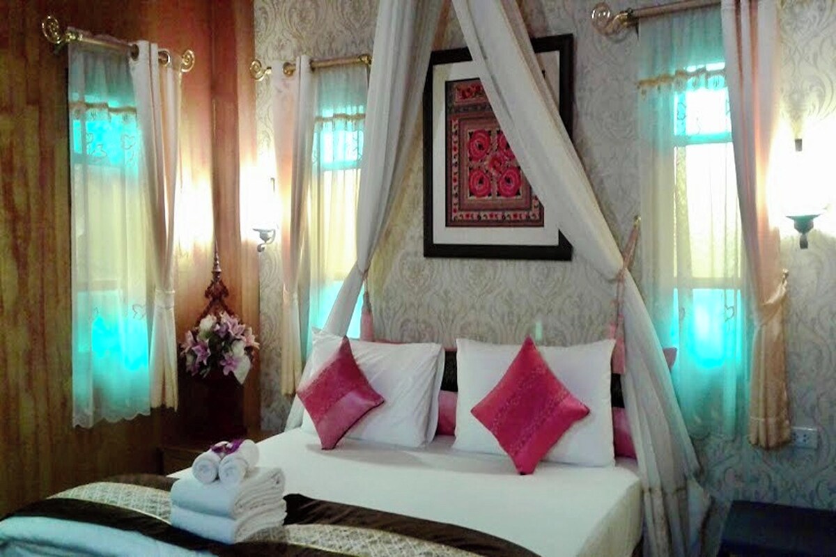 A bedroom with a canopy bed, a bedside table with a vase of flowers, and a framed picture on the wall.