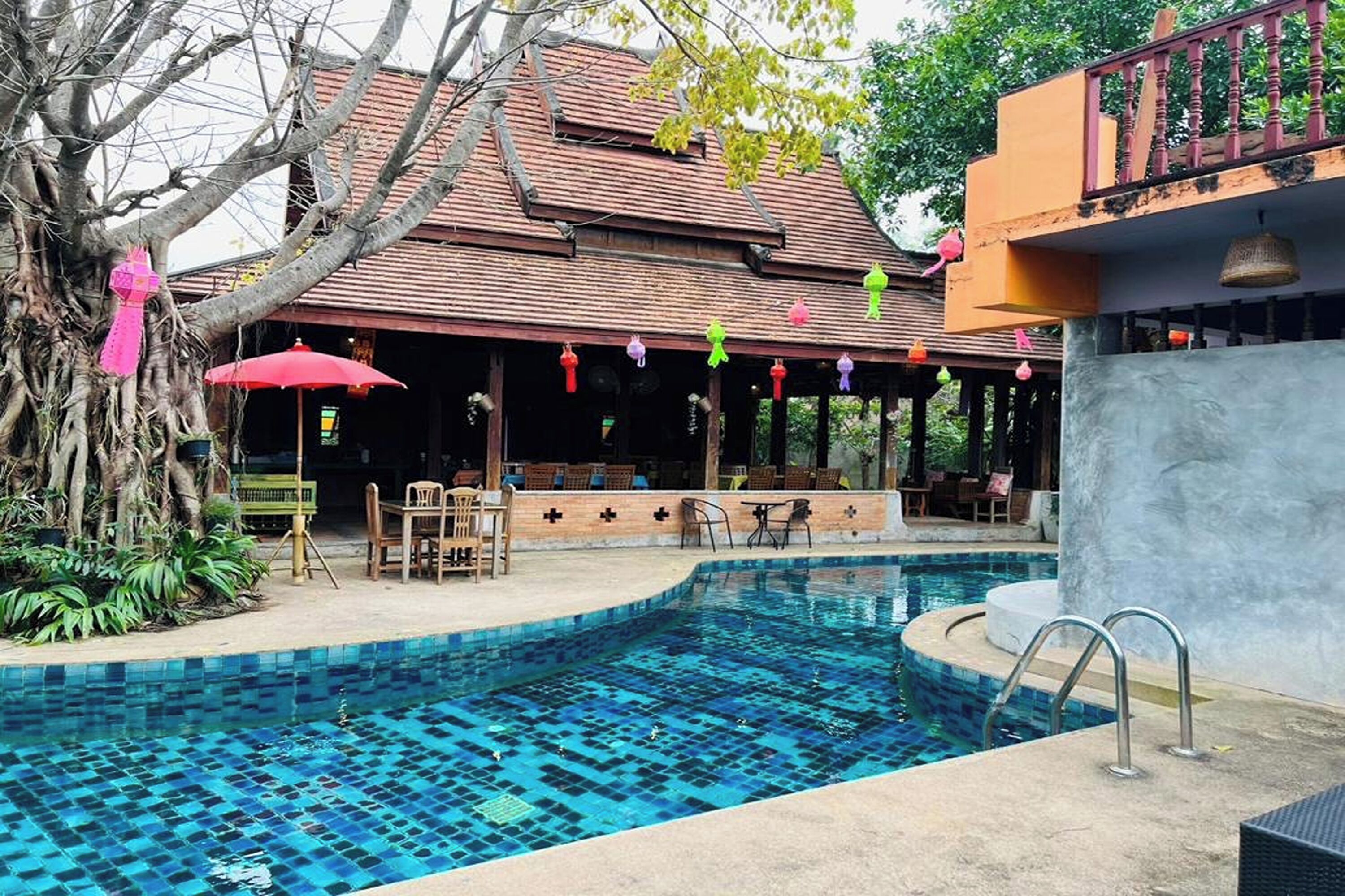 A swimming pool with a tiled pattern, surrounded by outdoor seating and a covered area with a red roof.