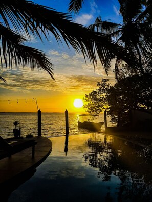 A sunset view over a calm body of water with a boat docked near the shore, surrounded by palm trees and a clear sky. - Hiru Lagoon Negombo (Negombo)